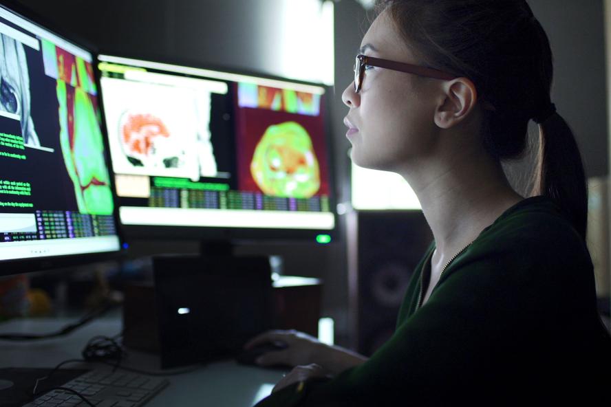 Woman looking at computer monitors with images of brains